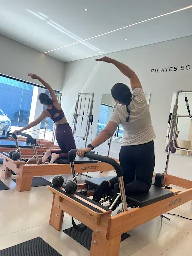 Alunas fazem alongamento lateral sobre aparelhos Reformer Equipilates em aula em grupo no Pulse Pilates Fit